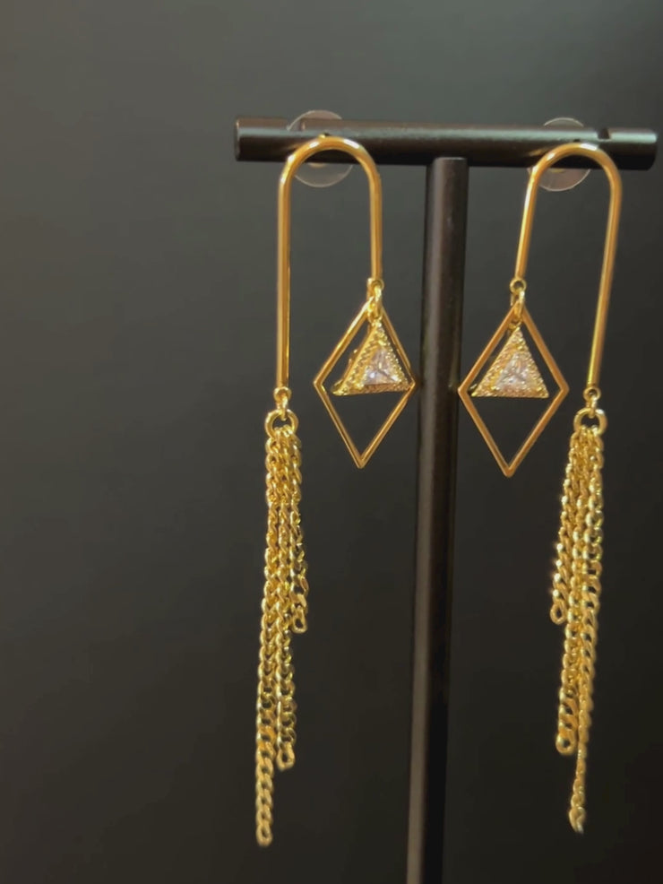 DIPHDA Cosmic Waterfall Earrings with cubic zirconia triangle charms and gold chain fringe, displayed against a celestial backdrop